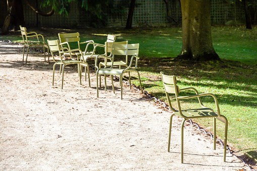 Typical green metal lawn chairs scattered alongside an alley of the Luxembourg garden in Paris, France.