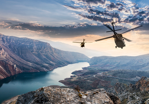 Two flying Sikorsky Uh-60 Blackhawk military helicopters flying against sunset over valley