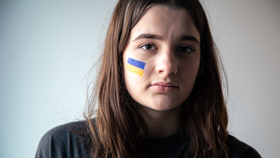 Ukrainian girl with a painted flag of Ukraine on her face, the concept of war in Ukraine, patriotism.