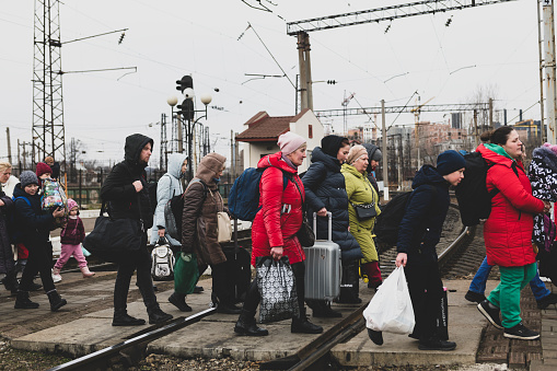 Lviv, Ukraine - March 3, 2022: Having just disembarked a train, people walk with their luggage across the tracks in Lviv.
