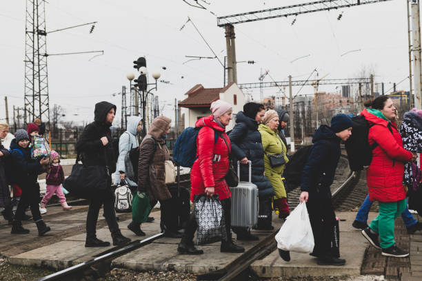 Ukrainians arriving at the train station in Lviv, Ukraine Lviv, Ukraine - March 3, 2022: Having just disembarked a train, people walk with their luggage across the tracks in Lviv. lviv photos stock pictures, royalty-free photos & images