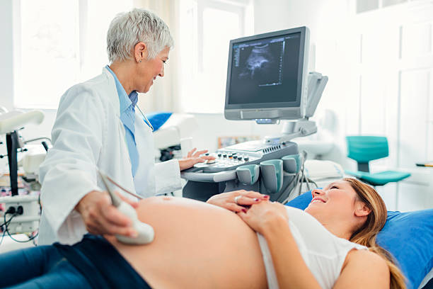 Ultrasound Examination In Doctors Office Pregnant woman and her male doctor in a consultation. Woman lying down while her doctor doing ultrasound examination. Young woman looking at her doctor. gynecologist photos stock pictures, royalty-free photos & images