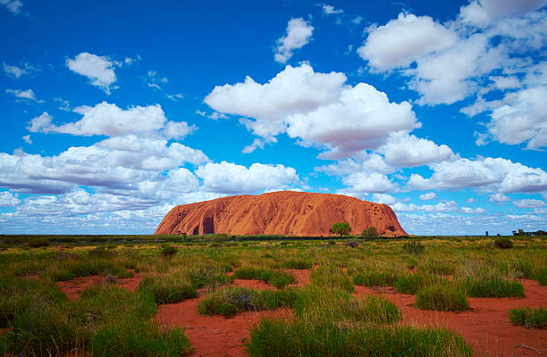 Uluru Scenic Australian Northern Territory Uluru, Northern Territory, Australia - March 29, 2016: Fluffy clouds drift over Uluru (also known as Ayers Rock) in the Australian Outback. A genuine Wonder of the Natural World (and a UNESCO World Heritage Site), it's also a sacred place to the local Anangu people. bush land photos stock pictures, royalty-free photos & images