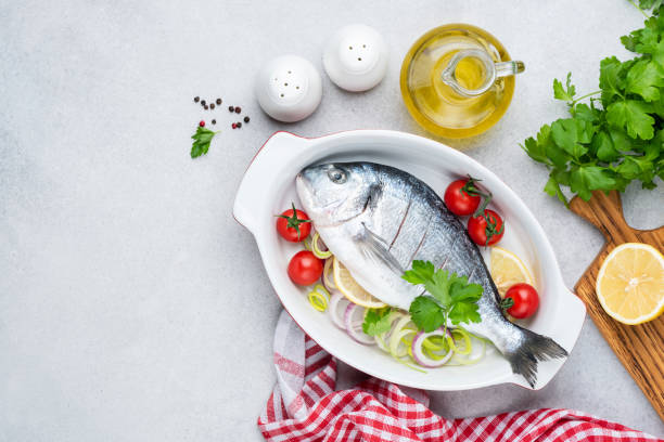 Uncooked dorado fish with vegetables in ceramic dish stock photo