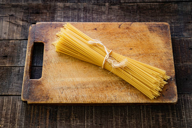 Uncooked spaghetti Spaghetti bundle on rustic wooden cutting board on dark brown table uncooked pasta stock pictures, royalty-free photos & images