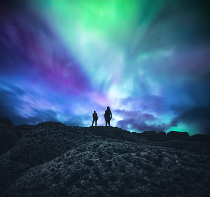 Man and woman standing in the middle of an Icelandic wilderness and watching aurora borealis.