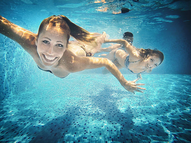 Underwater fun. Group of mid 20's people taking underwater selfies in a swimming pool. There are two girls and a guy in foreground, keeping airtight, smiling and looking at camera. woman snorkeling stock pictures, royalty-free photos & images