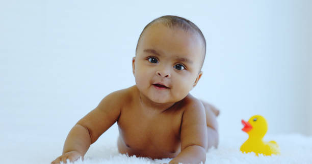 Undressed African American baby is lying on white carpet in room at home. infant growth. movement of child physical development. Caring for children health to be healthy. Toddler curiosity evolution stock photo