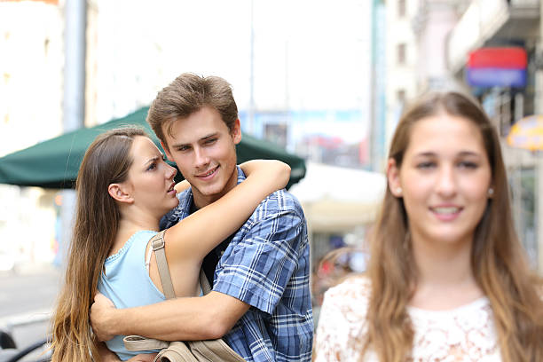 Unfaithful man hugging his girlfriend and looking another Unfaithful man hugging his girlfriend while is looking another one in the street envy stock pictures, royalty-free photos & images