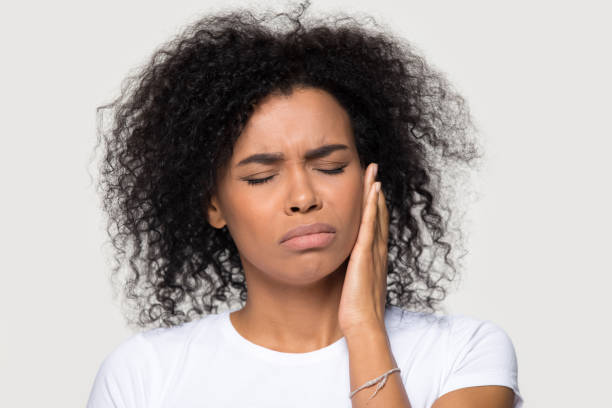 Unhappy African American woman suffering from tooth pain close up Unhappy upset African American woman suffering from tooth pain close up, teeth problem, frustrated sad young female feeling painful toothache, touching cheek, isolated on studio background human jaw bone stock pictures, royalty-free photos & images