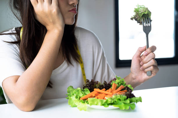 Unhappy asian women is on dieting time looking at vegetable on the fork. stock photo