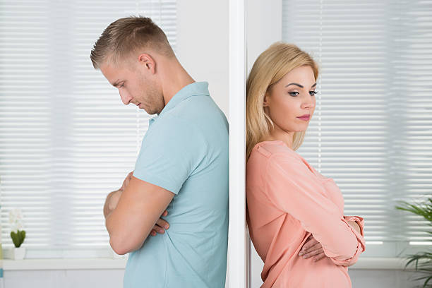 Unhappy Couple Standing Back To Back At Home Side view of unhappy young couple standing back to back at home images of divorce stock pictures, royalty-free photos & images