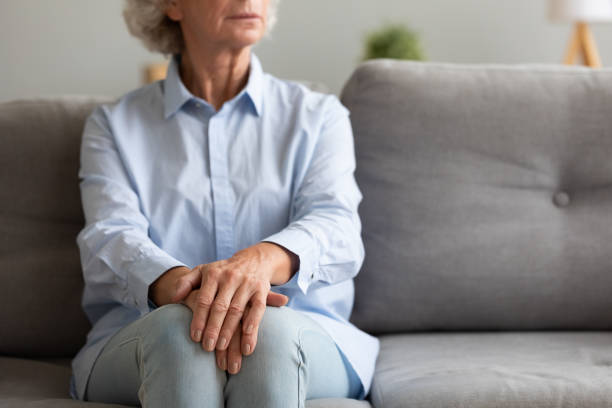 Unhappy depressed senior woman sit alone on sofa, closeup view Unhappy depressed old senior woman sit alone on sofa with hands folded thinking of loneliness worried of disease or retirement problems feel anxiety grief suffer from arthritis concept, close up view loneliness stock pictures, royalty-free photos & images