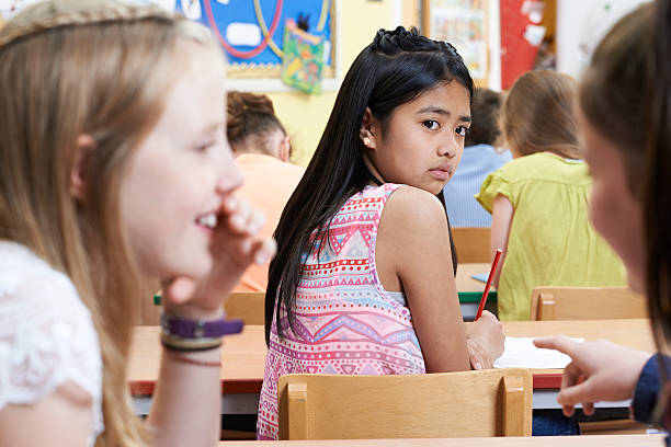 Unhappy Girl Being Gossiped About By School Friends In Classroom Unhappy Girl Being Gossiped About By School Friends In Classroom philippine girl stock pictures, royalty-free photos & images