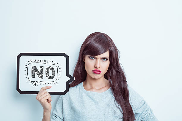 Unhappy young woman holding speech bubble Portrait of young woman wearing grey jumper, holding a speech bubble with word "no". Studio shot, white background. rejection photos stock pictures, royalty-free photos & images