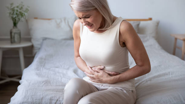 Unhealthy mature woman holding belly, suffering from pain Unhealthy mature woman holding belly, feeling discomfort, health problem concept, unhappy older female sitting on bed, suffering from stomachache, food poisoning, gastritis, abdominal pain, climax stomachache stock pictures, royalty-free photos & images