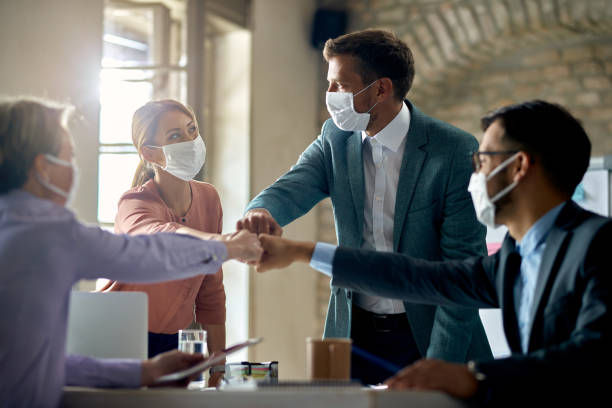 United business team with face masks colliding their fists on a meeting in the office. Group of colleagues wearing protective face masks and fist bumping while having business meeting during coronavirus pandemic. micro organism photos stock pictures, royalty-free photos & images