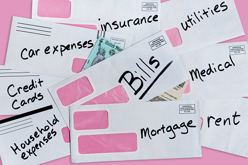 Stimulus check partially buried under multiple bills and envelopes with pink background and copy space