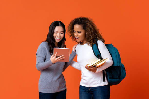 University students as friends looking at tablet computer Interracial university students as friends looking at tablet computer isolated on colurful orange background chinese girl hairstyle stock pictures, royalty-free photos & images