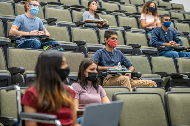 University students wearing masks in a lecture hall College students sitting in a lecture hall keeping social distance during the COVID-19 pandemic and wearing masks to protect from the transfer of germs. community colleges stock pictures, royalty-free photos & images