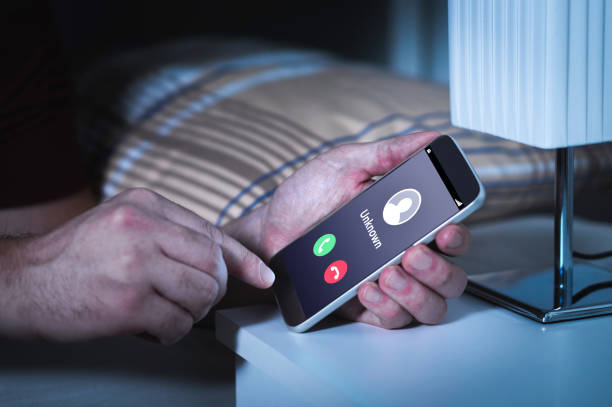 Unknown number calling in the middle of the night. Phone call from stranger. Person holding mobile and smartphone in bedroom bed home late. Unknown number calling in the middle of the night. Phone call from stranger. Person holding mobile and smartphone in bedroom bed home late. Unexpected call woke up. scammer stock pictures, royalty-free photos & images