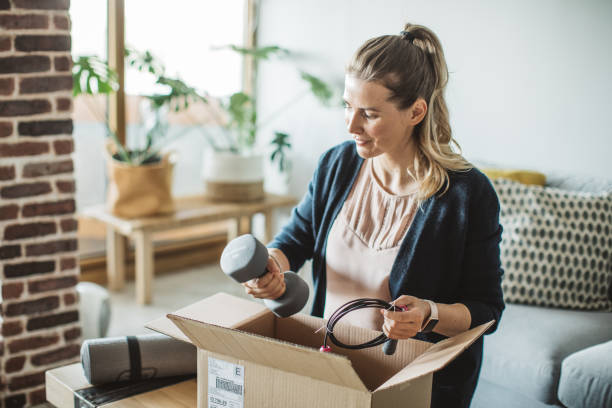 Unpacking workout equipment delivery in pandemic situation Women unpacking workout equipment ordered online while in home isolation during quarantine. Stay home we deliver sign on box. Sports Package stock pictures, royalty-free photos & images