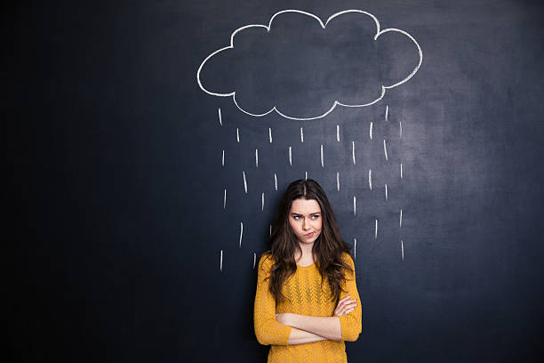 Unpleased woman with raincloud drawn over her on blackboard background Unpleased young woman with raincloud drawn over her on a blackboard background standing with arms crossed disappointment stock pictures, royalty-free photos & images
