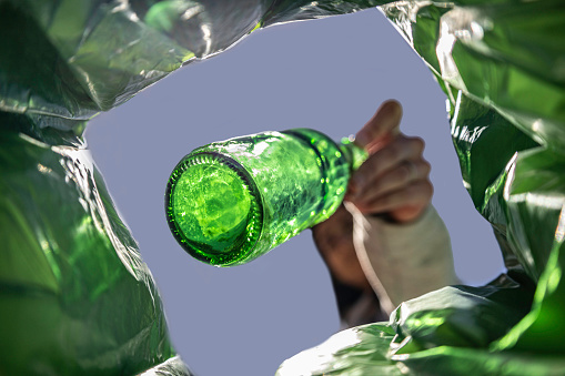 Unrecognisable woman recycles beer bottle in green container for glass