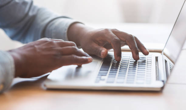 unreconocible hombre afroamericano escribiendo en el teclado de la computadora portátil en la oficina - mecanografiar fotografías e imágenes de stock