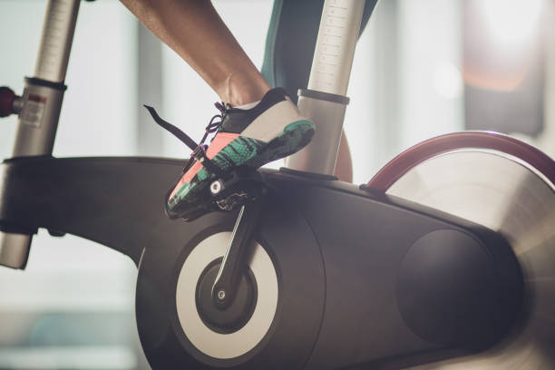 Unrecognizable athletic legs during exercising training in a health club. Close up of unrecognizable female athlete exercising on exercise bike in a gym. peloton stock pictures, royalty-free photos & images