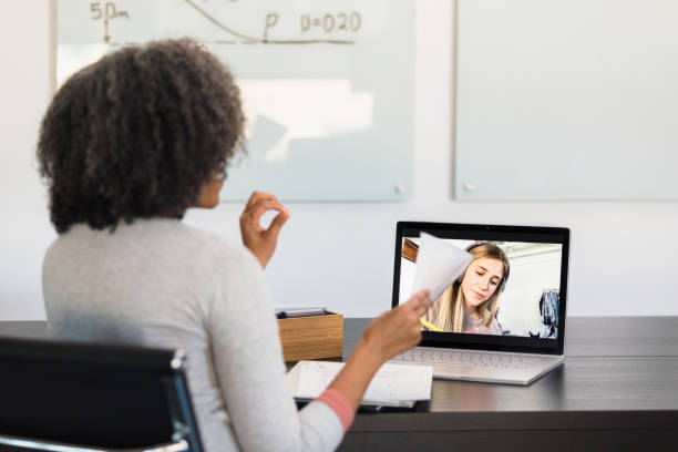 Unrecognizable female tutor helps young adult woman via video conferencing stock photo
