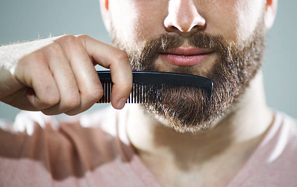 Unrecognizable man combing his beard Closeup of unrecognizable caucasian man combing his beard and mustach with small black comb.He has neat,fully grown brown beard and mustache.Studio shot over gray background. ,=Front view. neat photos stock pictures, royalty-free photos & images