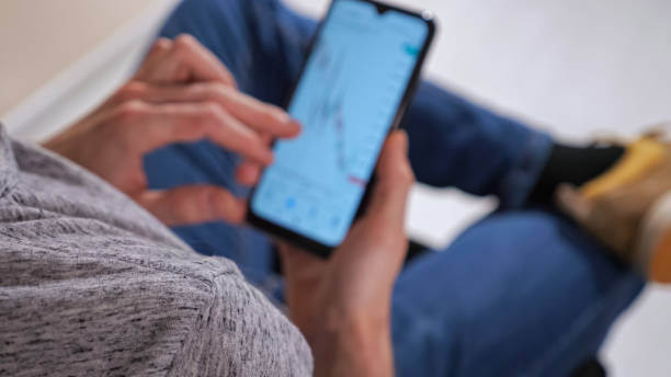 Unrecognizable man with phone examines stock market charts analysis stock photo