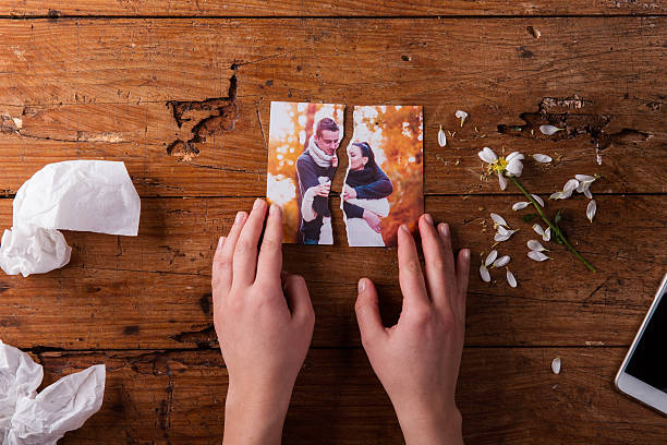 Unrecognizable sad woman holding torn picture of couple in love. Unrecognizable woman holding torn picture of couple in love. Ended relationship. Crying.Valentines day composition. Studio shot on brown wooden background. couple relationship photos stock pictures, royalty-free photos & images