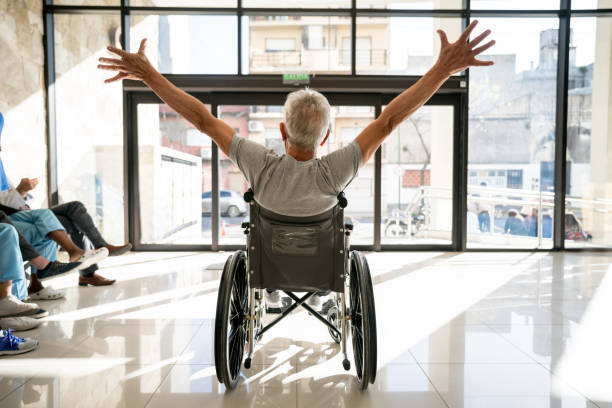 Unrecognizable senior patient leaving the clinic on a wheelchair with his arms up Backview of unrecognizable senior patient leaving the clinic on a wheelchair with his arms up leaving stock pictures, royalty-free photos & images