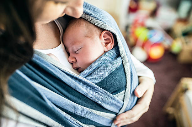 Unrecognizable young mother with her son in sling Close up of unrecognizable young mother with her newborn baby son in sling at home carrying stock pictures, royalty-free photos & images