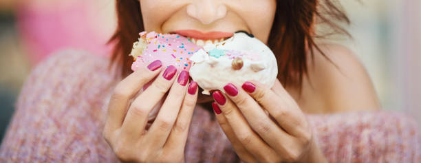 Unrecognizable young woman eating delicious donuts. Unrecognizable young woman eating donuts at city street. sugar food stock pictures, royalty-free photos & images