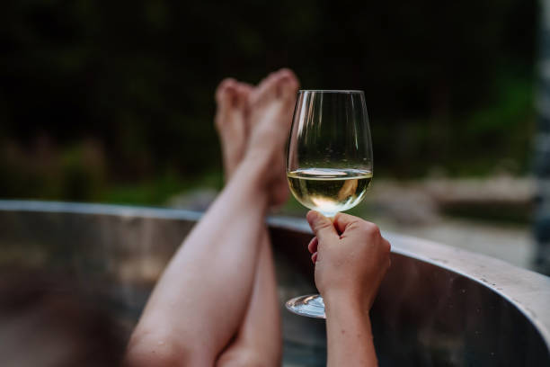 Unrecognizable young woman with feet up relaxing with glass of wine in hot tub outdoor in nature. stock photo