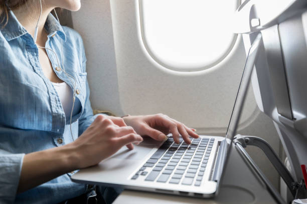Unrecognizable young woman works while in airplane Unrecognizable young businesswoman uses laptop while on airplane. She is on a business trip. plane window seat stock pictures, royalty-free photos & images