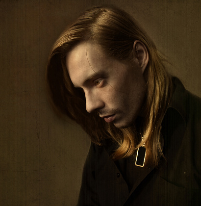Unshaven Man With Long Blond Hair In A Dark Room Stock Photo
