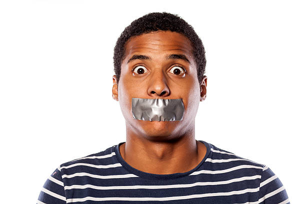 upset dark-skinned young man with adhesive tape over his mouth - plakband mond stockfoto's en -beelden