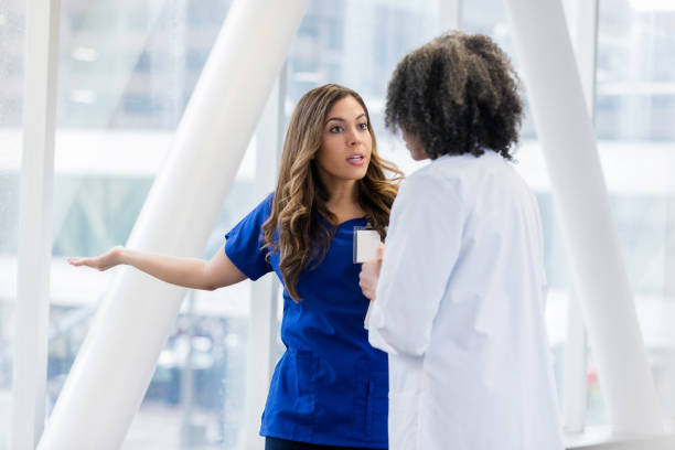 Upset female healthcare professional talks with colleage Female healthcare professionals disagree about a patient's diagnosis. A young female doctor argues with a mature female colleague. She gestures with a serious expression on her face. fighting stock pictures, royalty-free photos & images