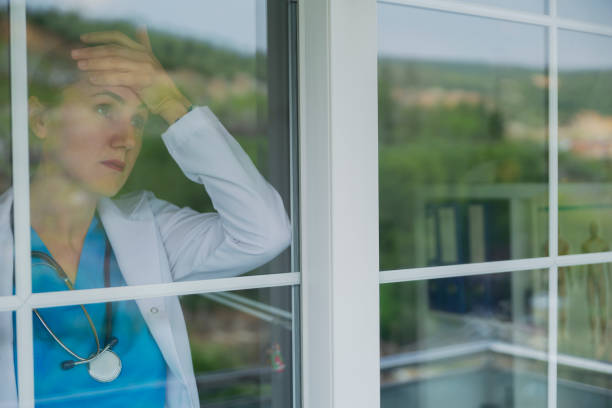 Upset female nurse standing in hospital window stock photo