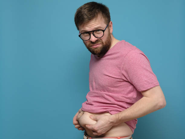 Upset man shows and holds with hands his excess fat on his stomach. Copy space. Overweight person. Healthy lifestyle concept. stock photo