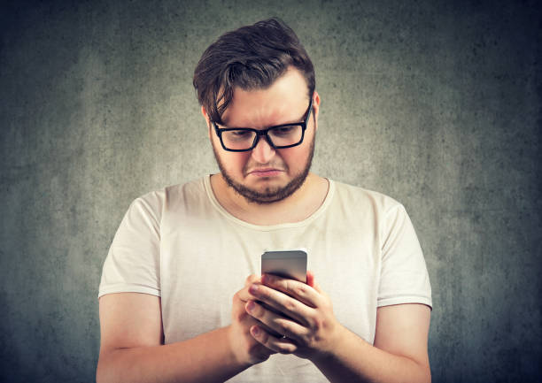 Upset man watching smartphone Casual sad young man received offensive message on smartphone looking upset and gloomy fat man looks at the phone stock pictures, royalty-free photos & images