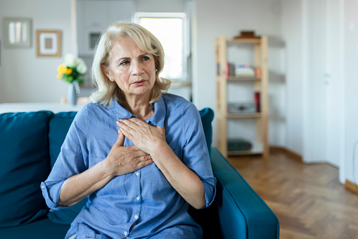 Senior Woman Suffering From Chest Pain While Sitting on Sofa at Home. Old Age, Health Problem, Vision and People Concept. Heart Attack Concept. Elderly Woman Suffering From Chest Pain Indoor