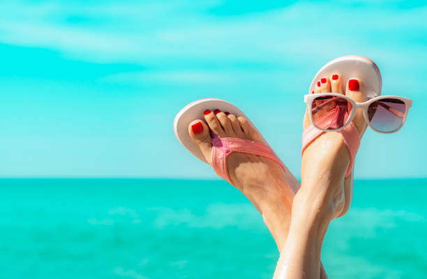 Upside woman feet and red pedicure wearing pink sandals, sunglasses at seaside. Funny and happy fashion young woman relax on vacation. Chill out girl at beach. Creative for tour agent. Weekend travel. stock photo
