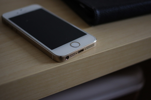 Used gold iPhone 5 with white panel and thunderbolt interface on light yellow wooden table