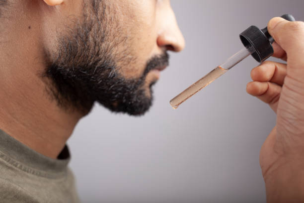 using beard grow oil on a dropper, minoxidil oung handsome guy showing a dropper filled with beard oil and going to apply it for beard growth on single color background Minoxidil stock pictures, royalty-free photos & images