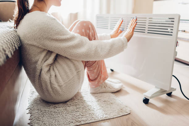 Using heater at home in winter. Woman warming her hands. Heating season. stock photo